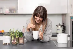 Frau steht mit einer Tasse Tee in der Küche