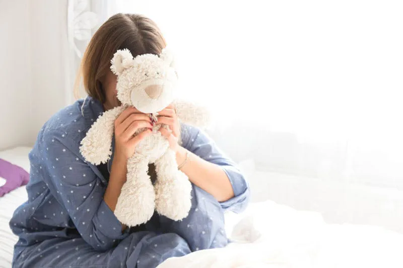 Frau hält sich Teddybären vor das Gesicht