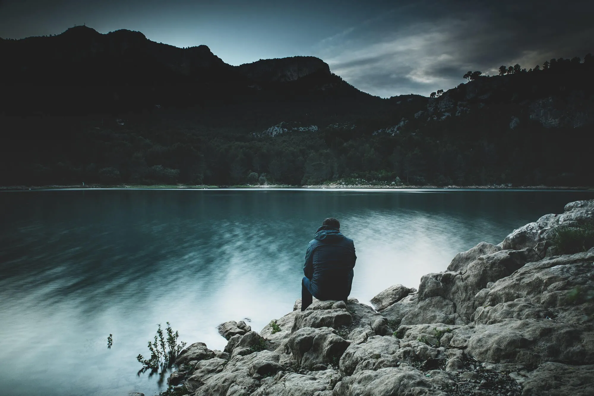 Mann, der in den Bergen auf einem Felsen vor einem See sitzt