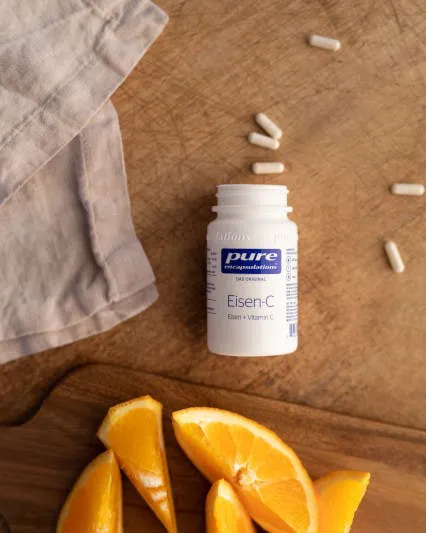 Eine Eisen-C-Bottle von Pure Encapsulation mit ein paar ausgeleerten Kapseln neben Orangenspalten