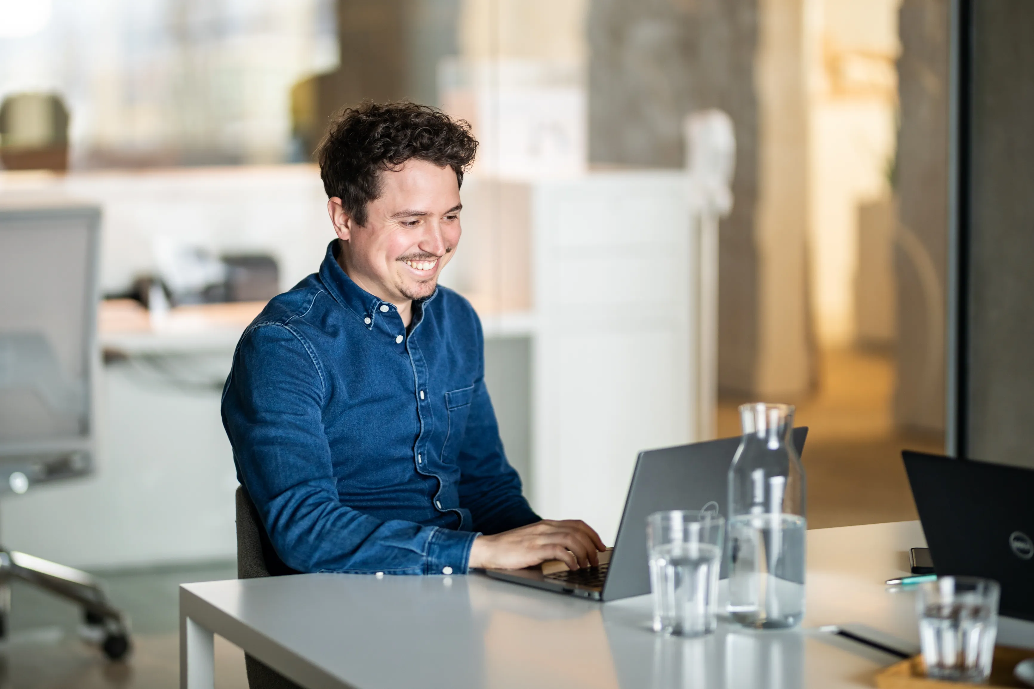 Lachender Mann sitzt an einem Tisch vor einem Laptop