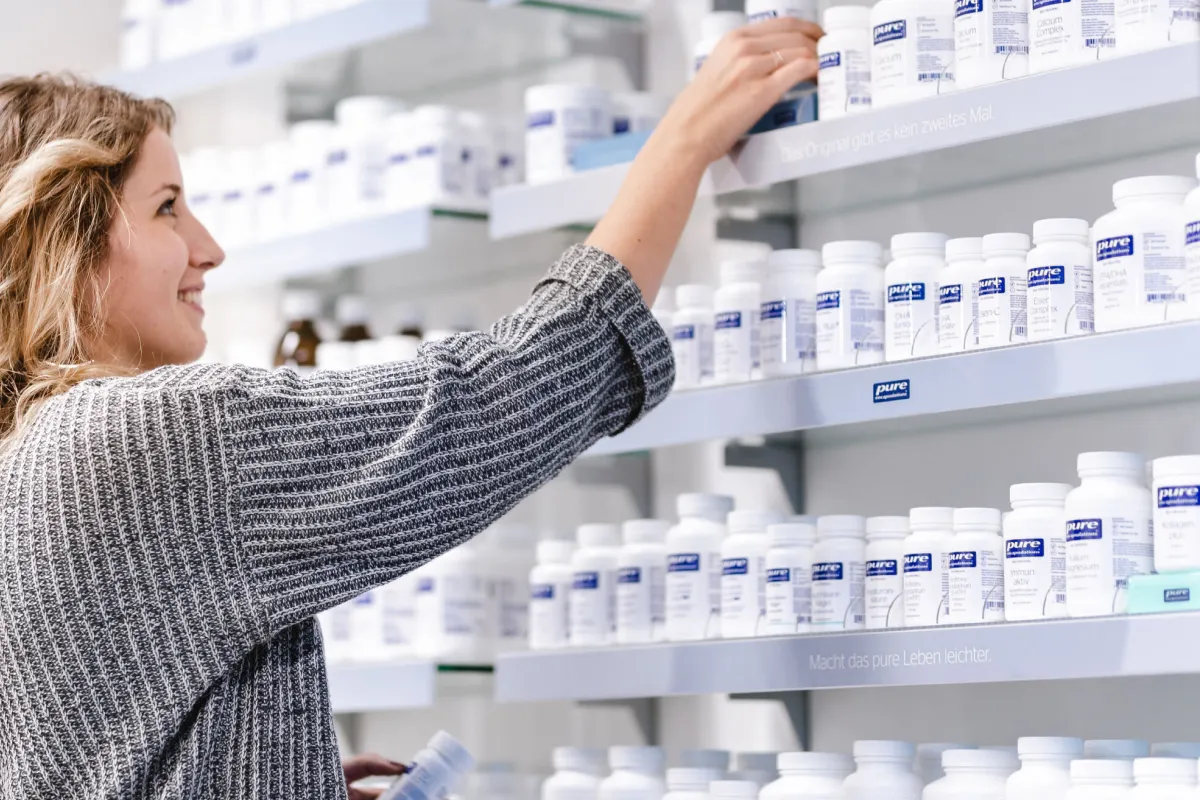 Frau steht vor einem Apothekenregal, das mit Nahrungsergänzungsmitteln von Pure Encapsulations gefüllt ist, und greift nach einer Packung