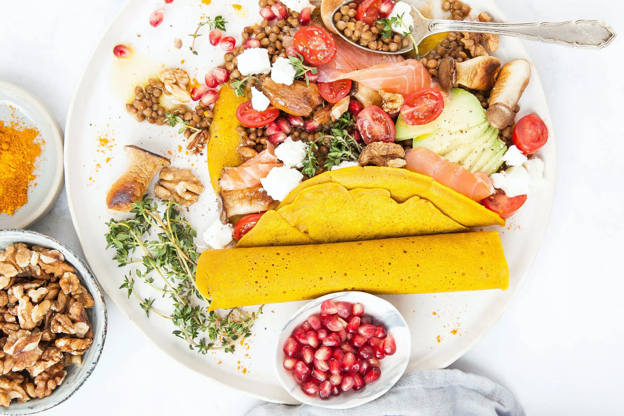üppig gefüllter Teller mit Linsensalat und Kurkuma-Crêpes, Walnüsse und Granatapfelkerne