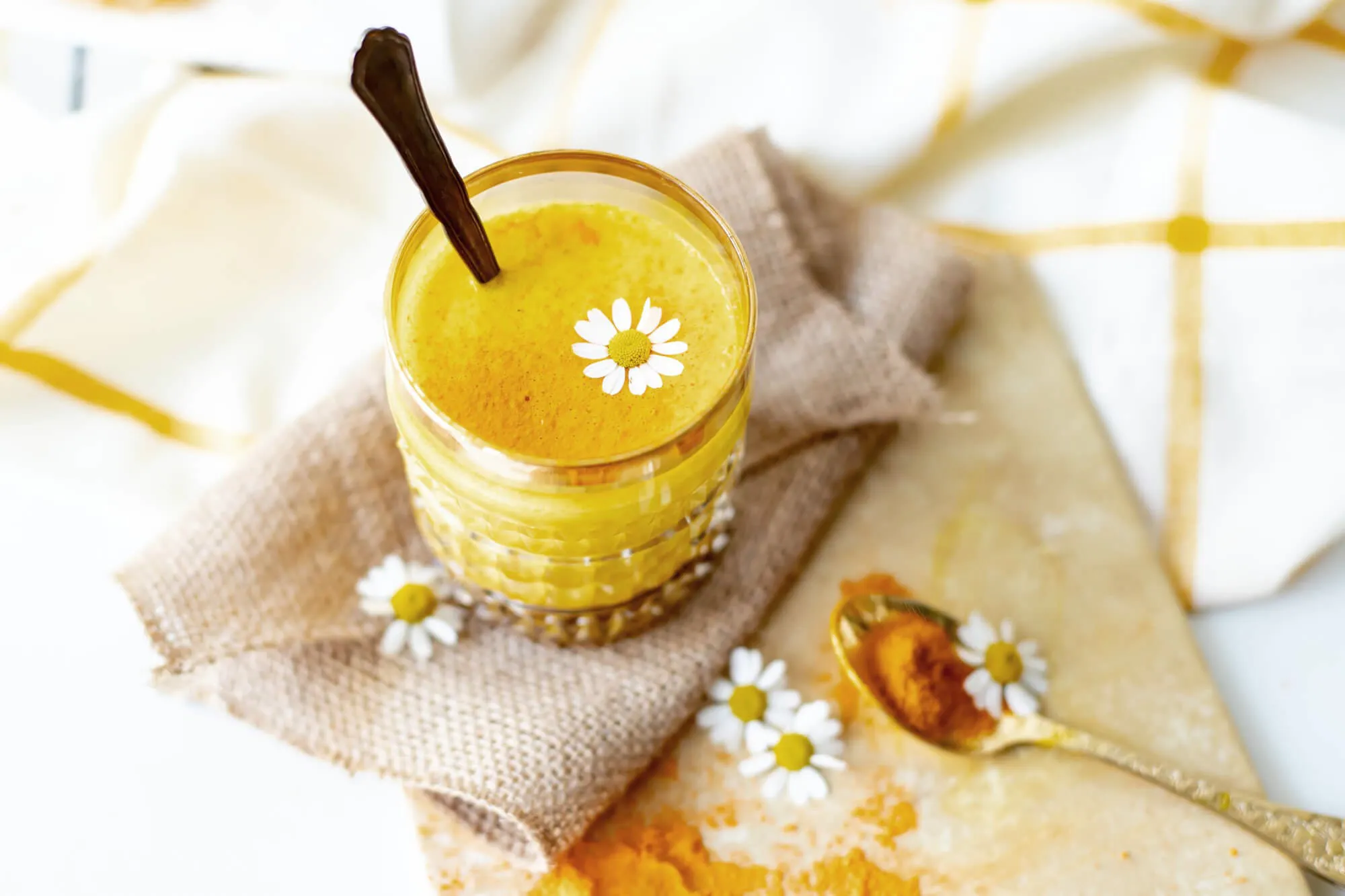 Ein Glas mit Curcuma-Latte und einem Löffel