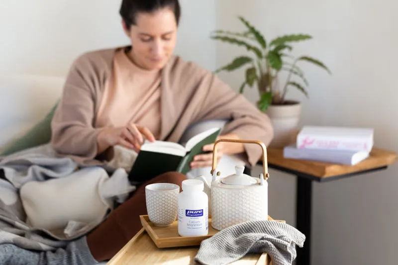 Frau mit Wärmeflasche und Buch auf Sofa