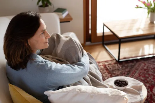 Frau in den Wechseljahren sitzt unter einer Decke auf der Couch