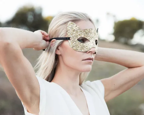 Frau bindet sich goldene Augenmaske um