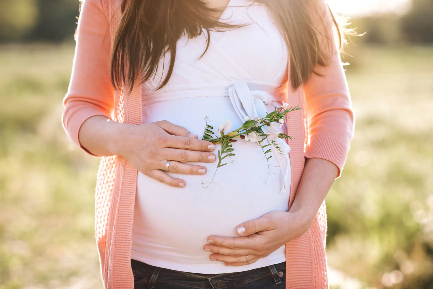 Frau hält ihren schwangeren Bauch und eine Blume