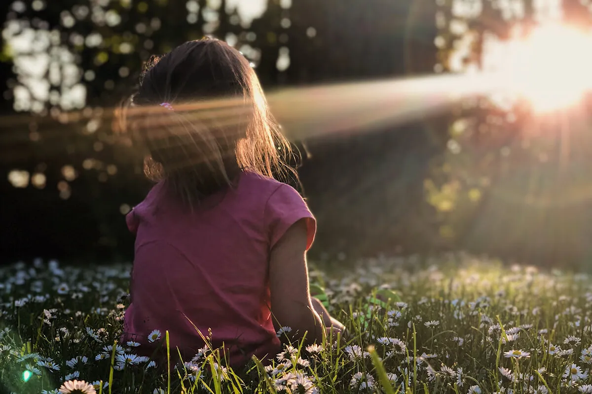 Kind sitzt in der Sonne auf einer Wiese