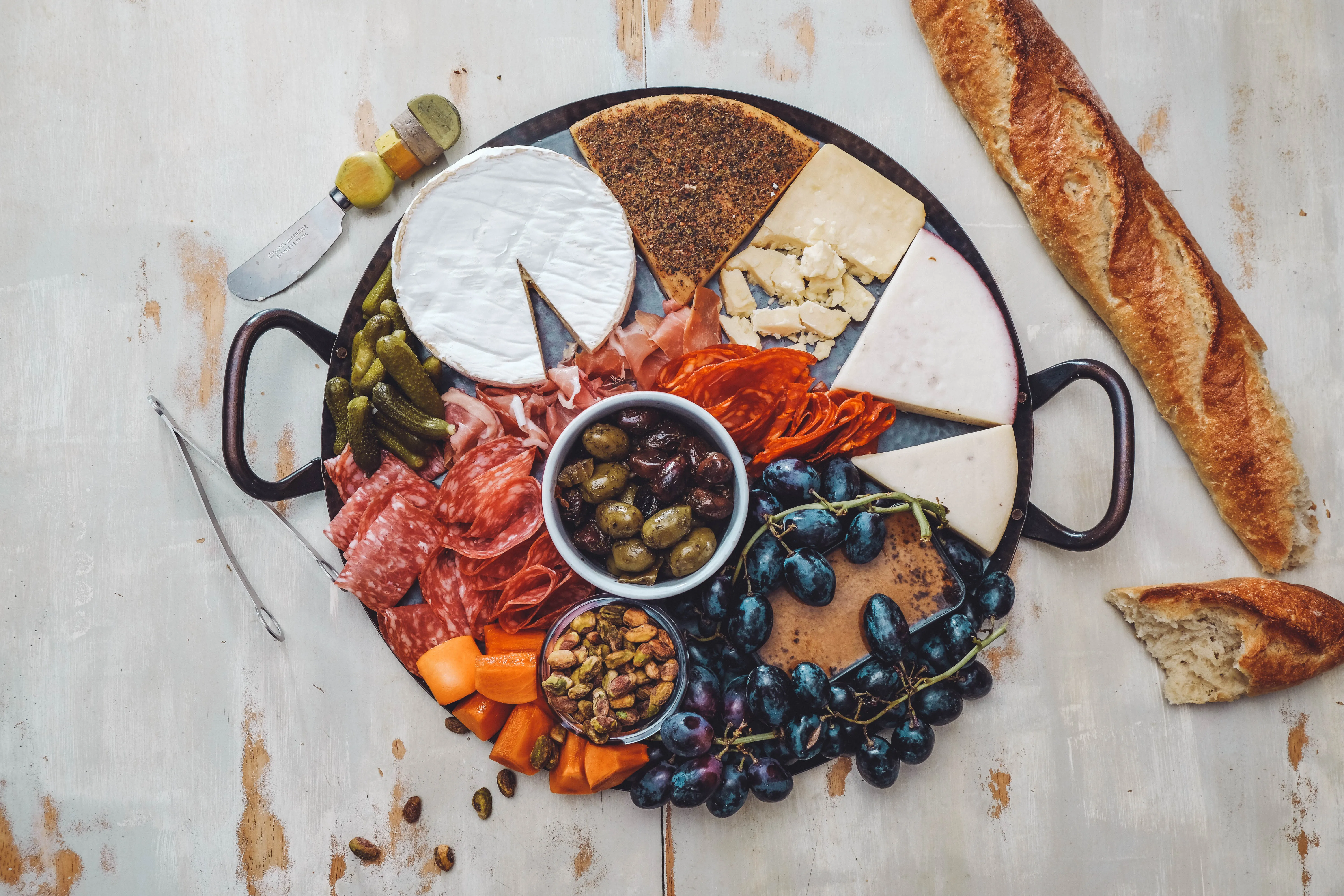 Käse, Brot, Wurst, Essiggurken, Oliven, Weintrauben und andere Dinge auf einem Teller