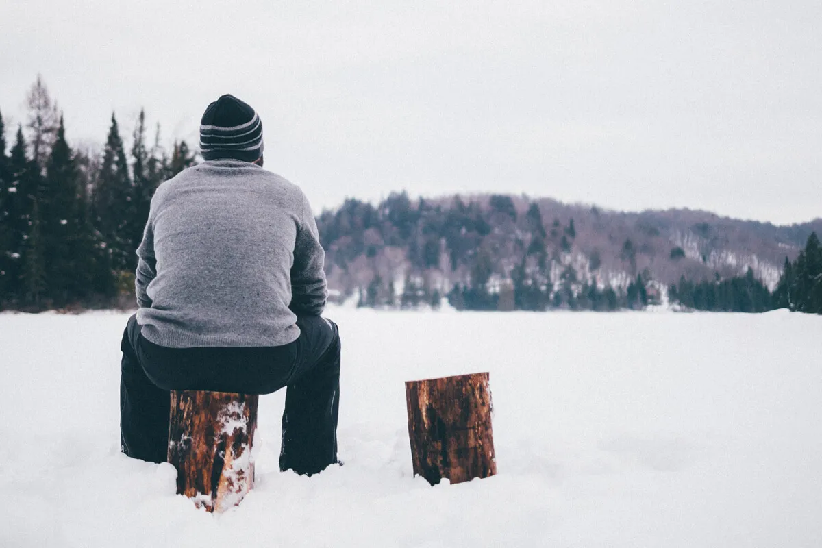 Mann sitzt im Schnee auf Holzpflock