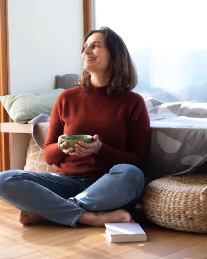 Frau sitzt mit einer Tasse Tee am Boden und lächelt